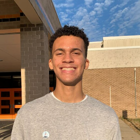 Colson smiles in a grey shirt on a sunny day with blue sky.